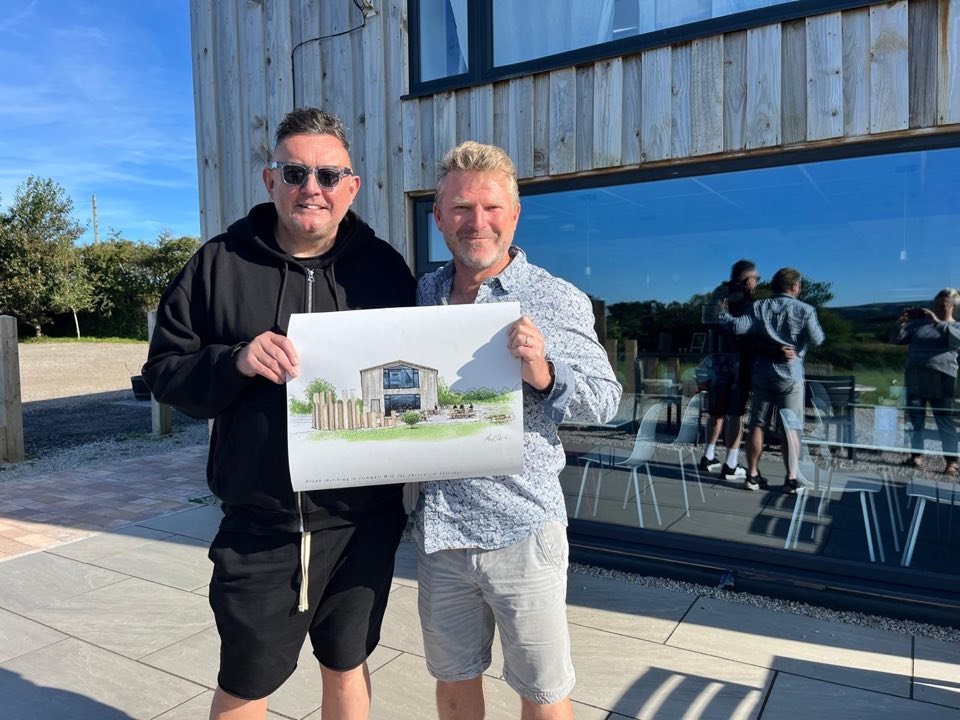 Damian with urban sketcher Phil Dean outside the Cornish Craft Barn, Phil holding a sketch of the Barn